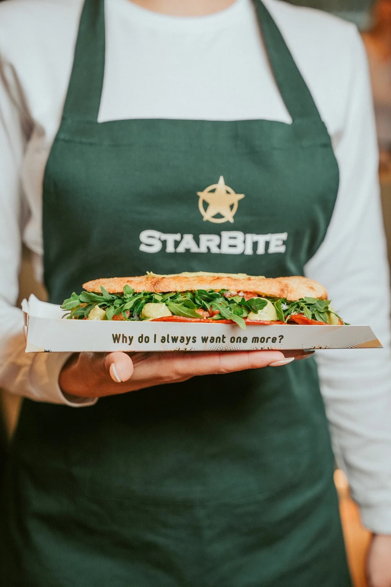 Staff in branded apron holding a sandwich
