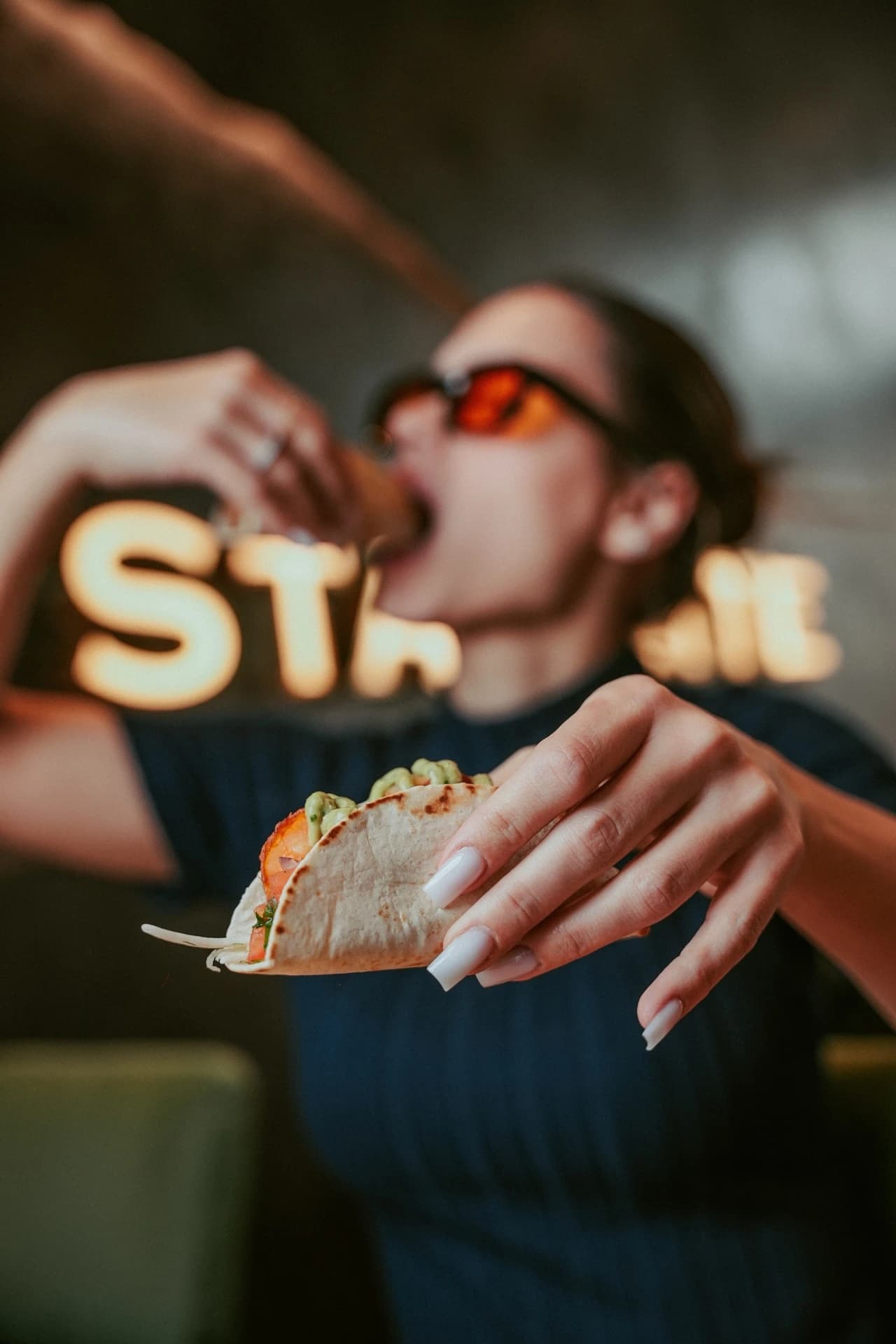 Woman eating a taco with neon sign behind